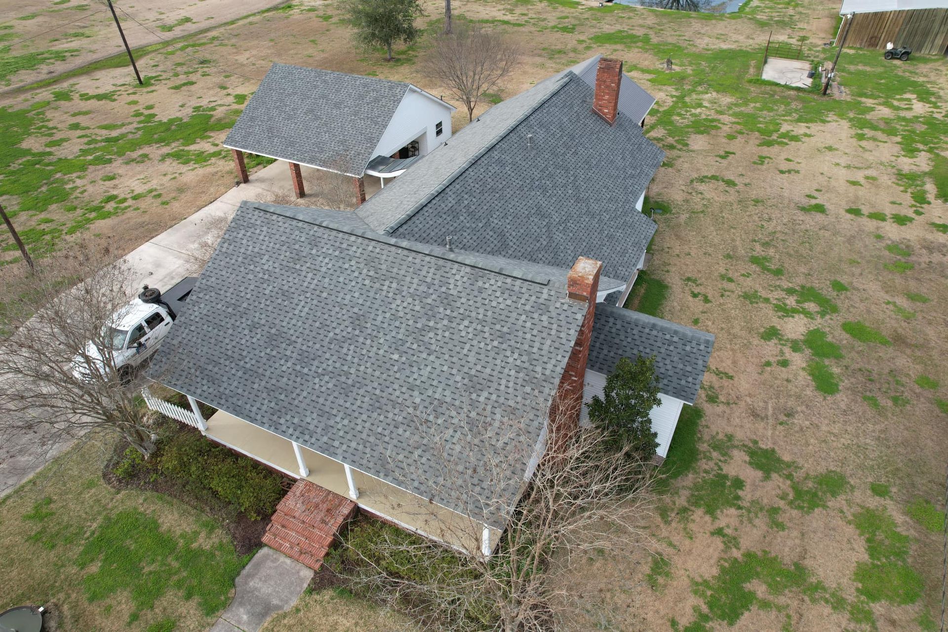 Aerial view of a house with gray roof, brick chimneys, and a small carport on a grassy lot