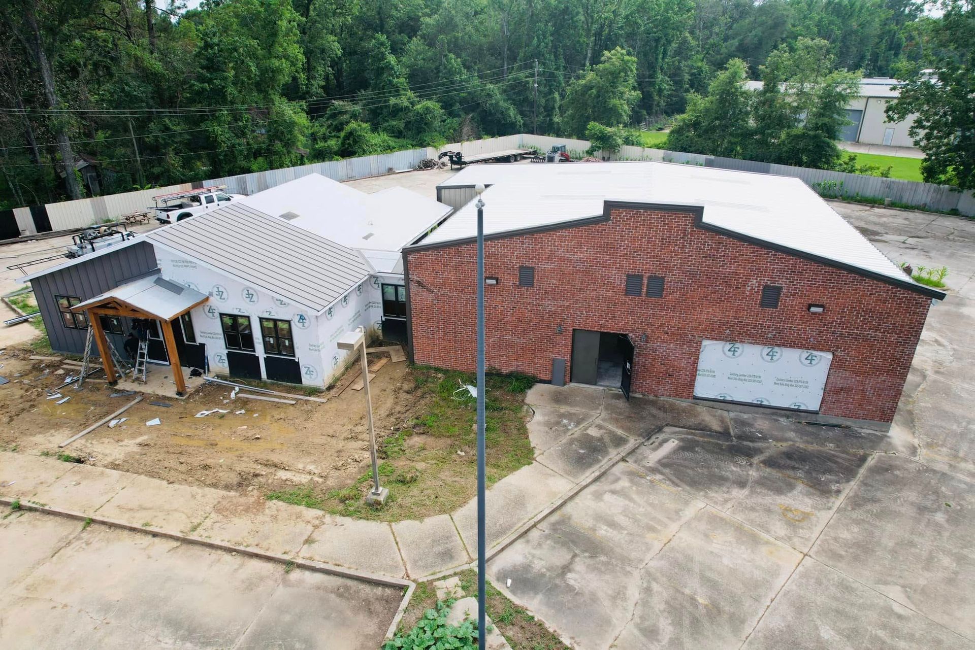 Aerial view of a damaged building with a collapsed white roof and a red brick wall beside an empty lot.