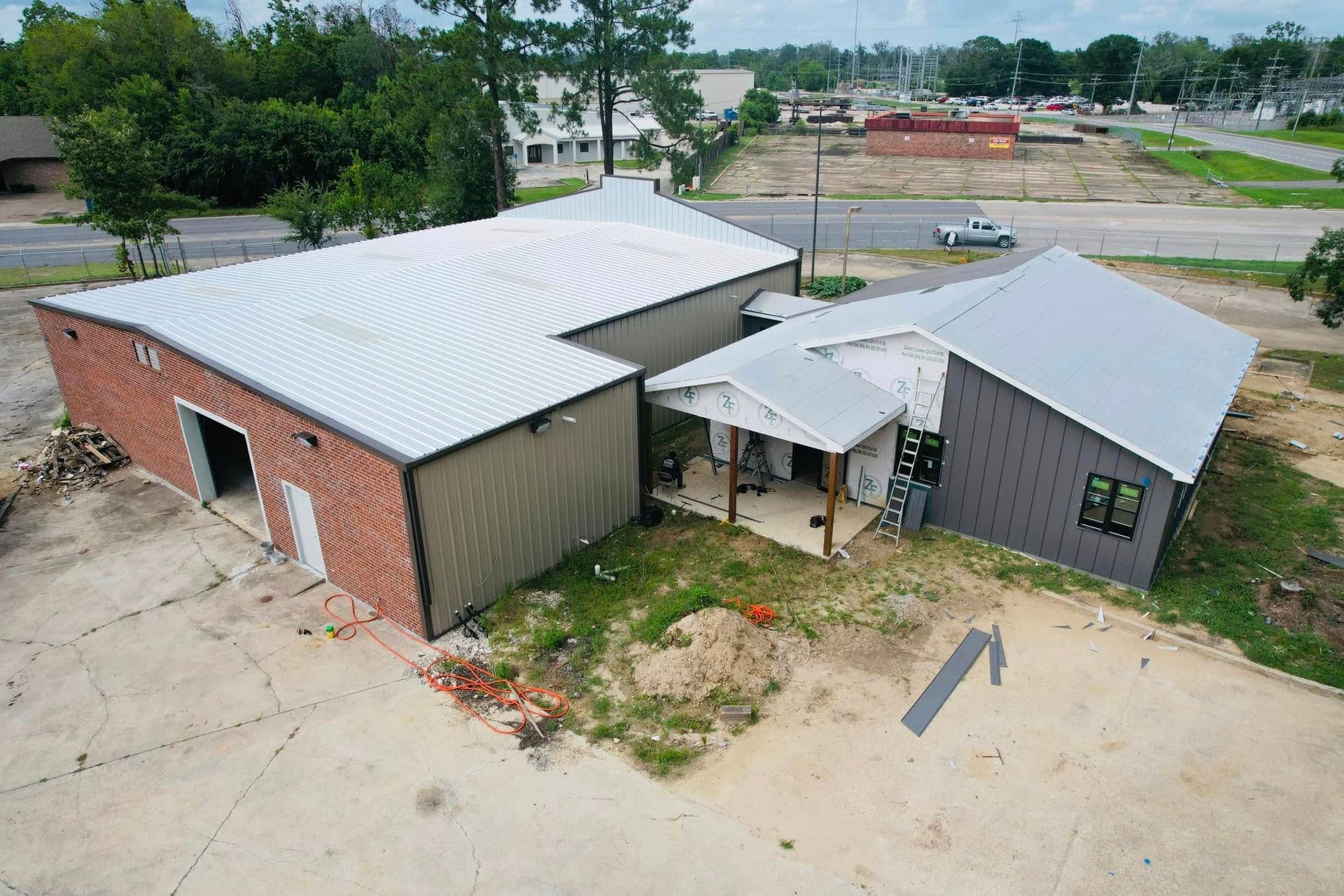 Aerial view of two connected buildings with metal roofs on a concrete lot and sparse grass.