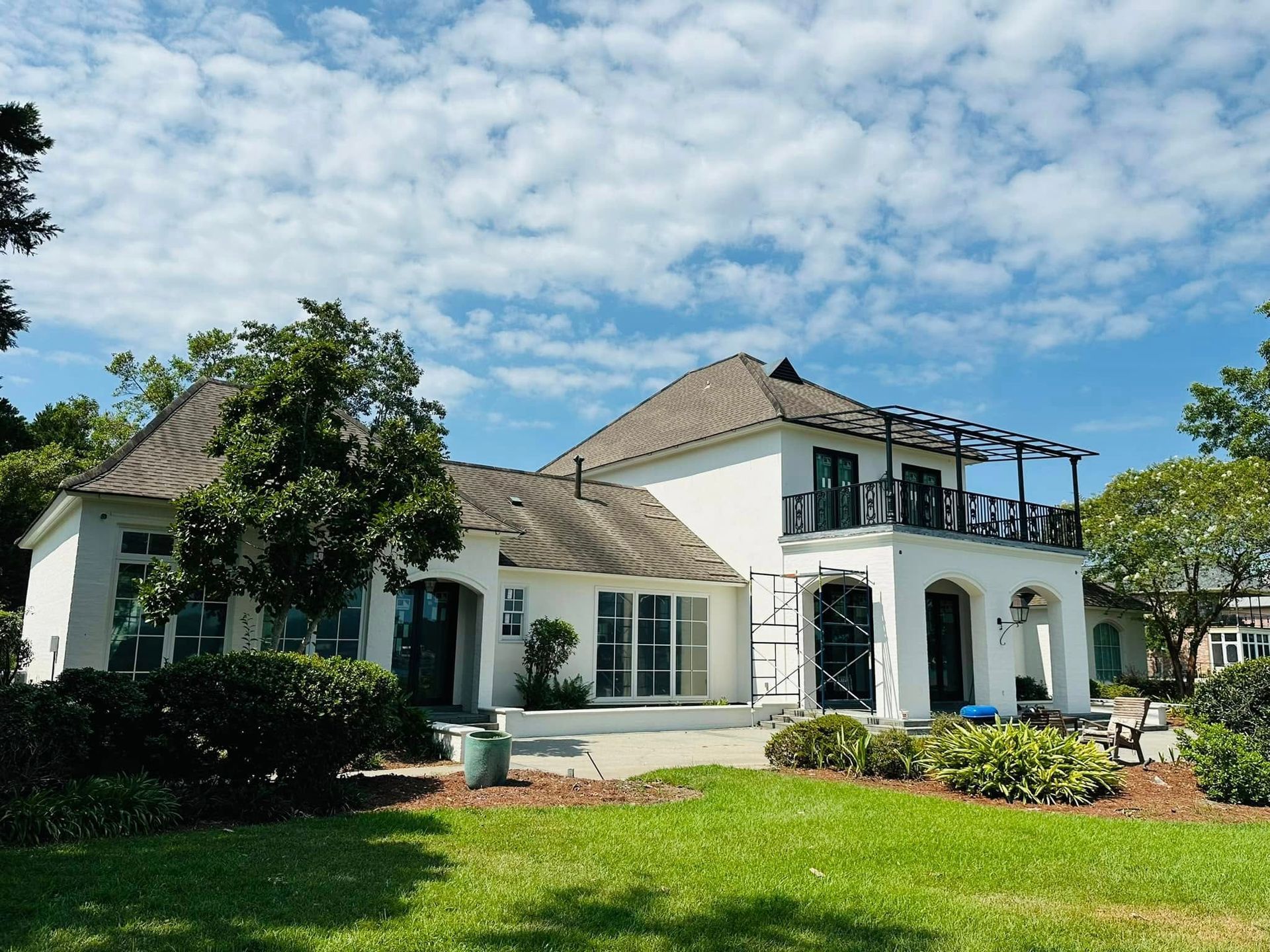 White two-story house with arched porch, dark roof, and lush green lawn under a cloudy blue sky
