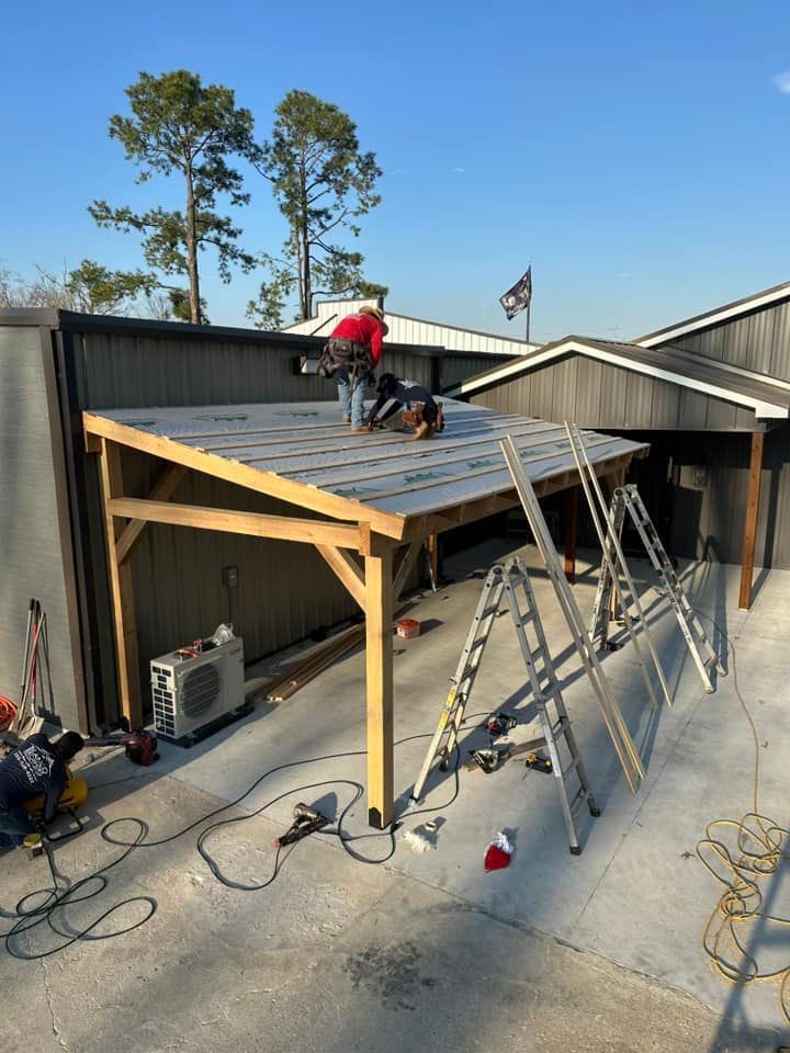 Worker installing roofing on a small metal shed with ladders and tools outside.