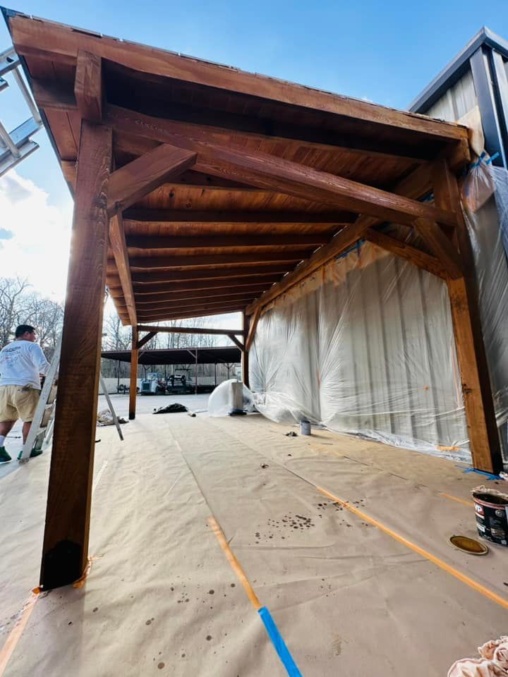 Wooden patio pergola under construction, with tarp-covered floor and side walls on a sunny day