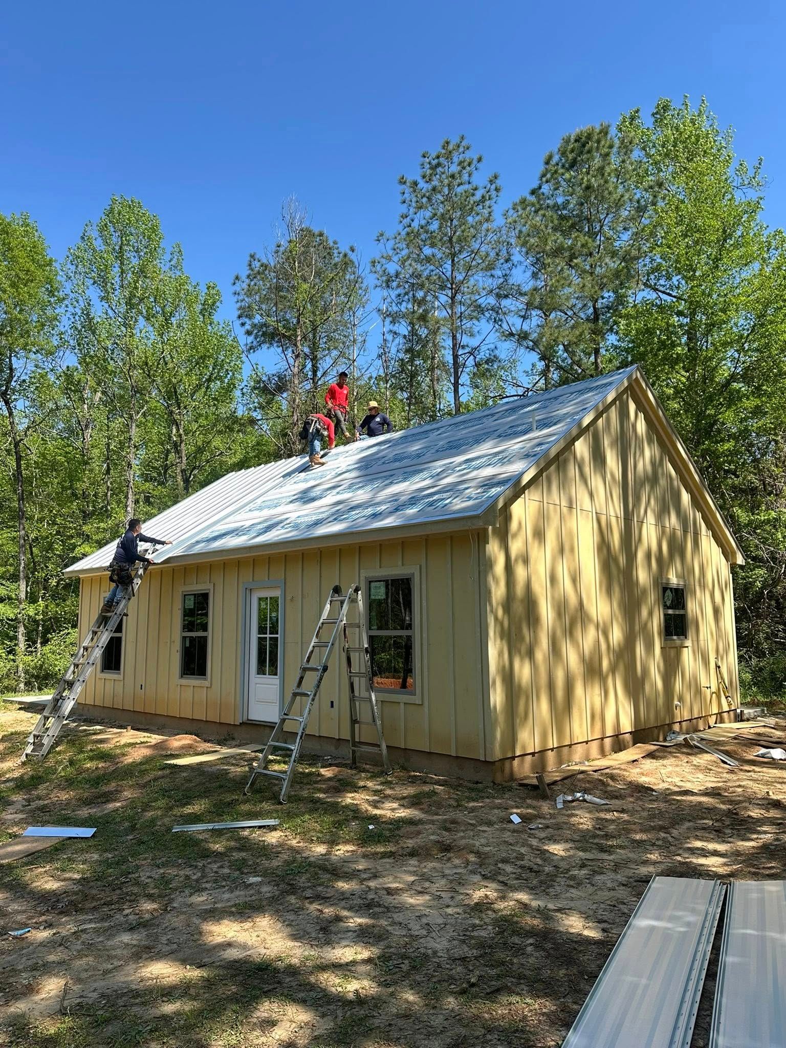 Yellow house under construction with workers on the roof in a wooded area