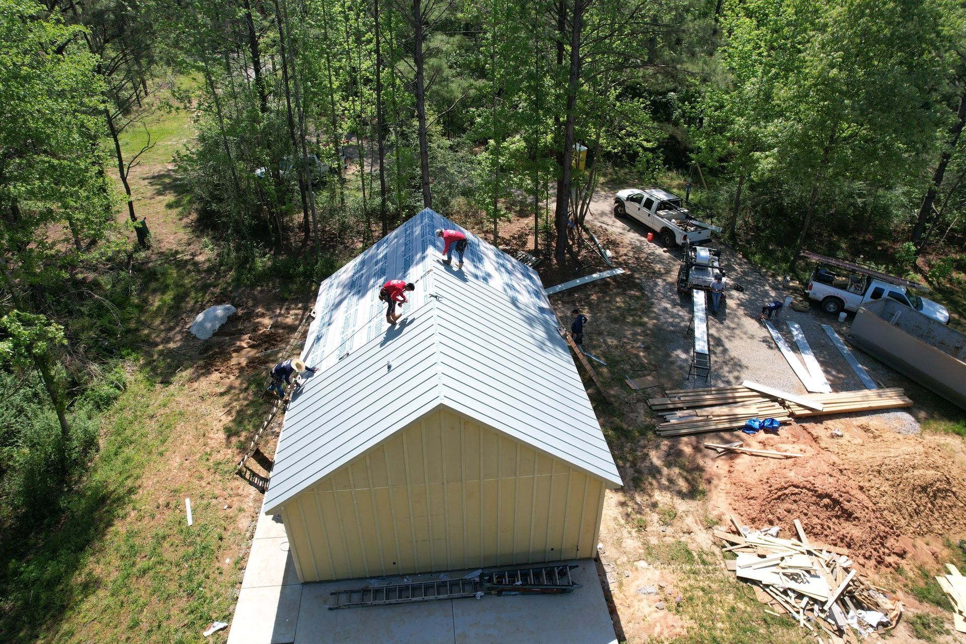 Aerial view of a house roof under construction, with workers and materials in a wooded area