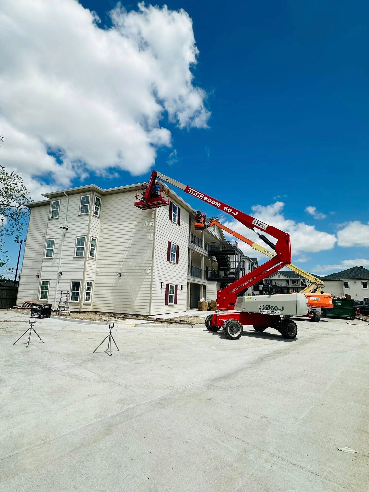 Red boom lift servicing the roof of a white apartment building on a sunny day