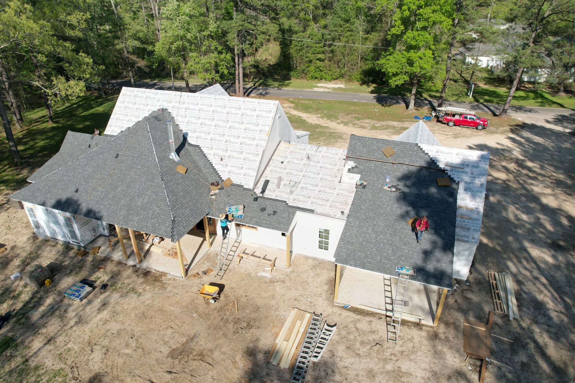 Aerial view of a house under construction with workers on the roof and dirt yard around it.