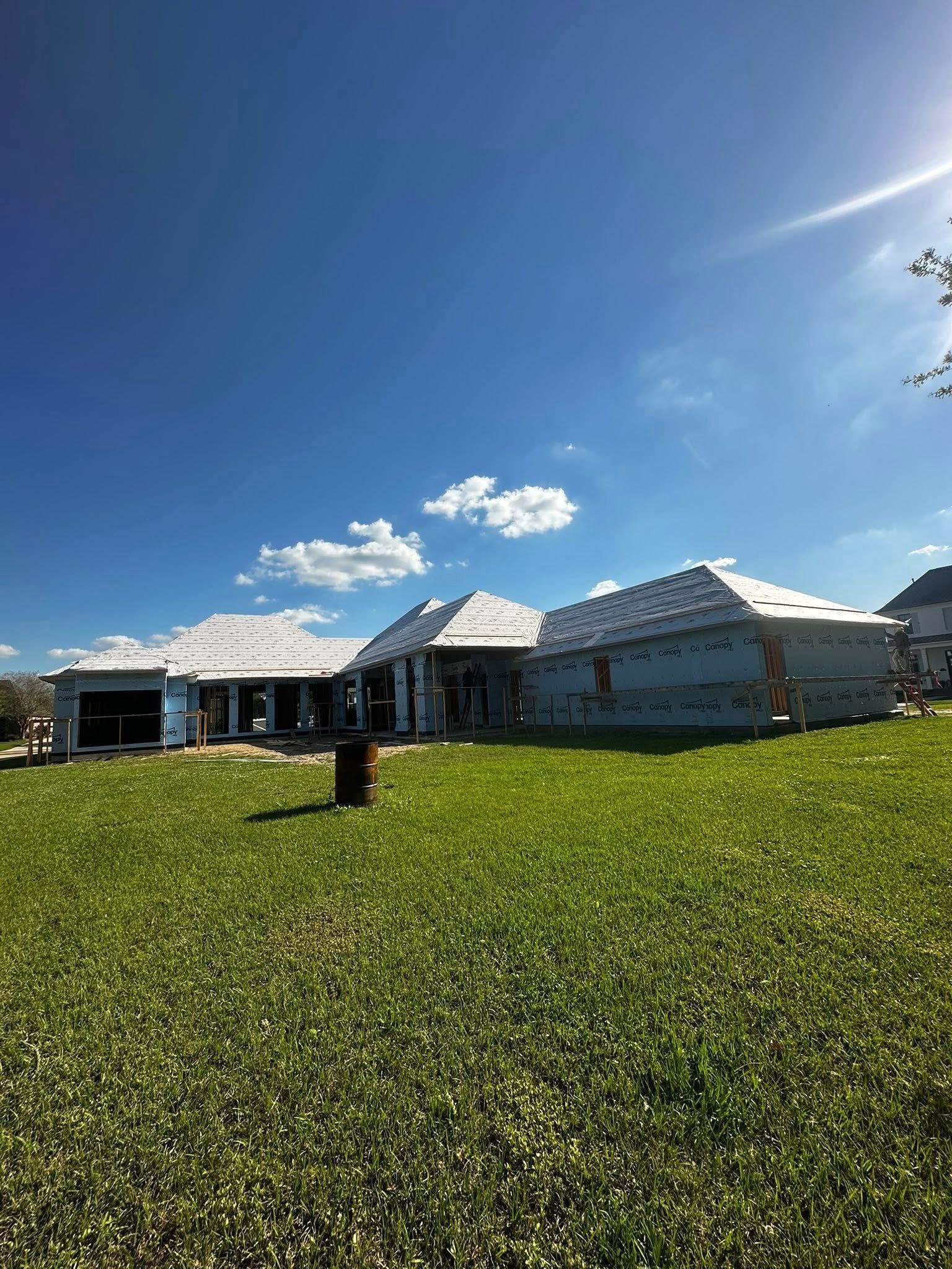 Wide grassy field in front of a white building under a bright blue sky with scattered clouds