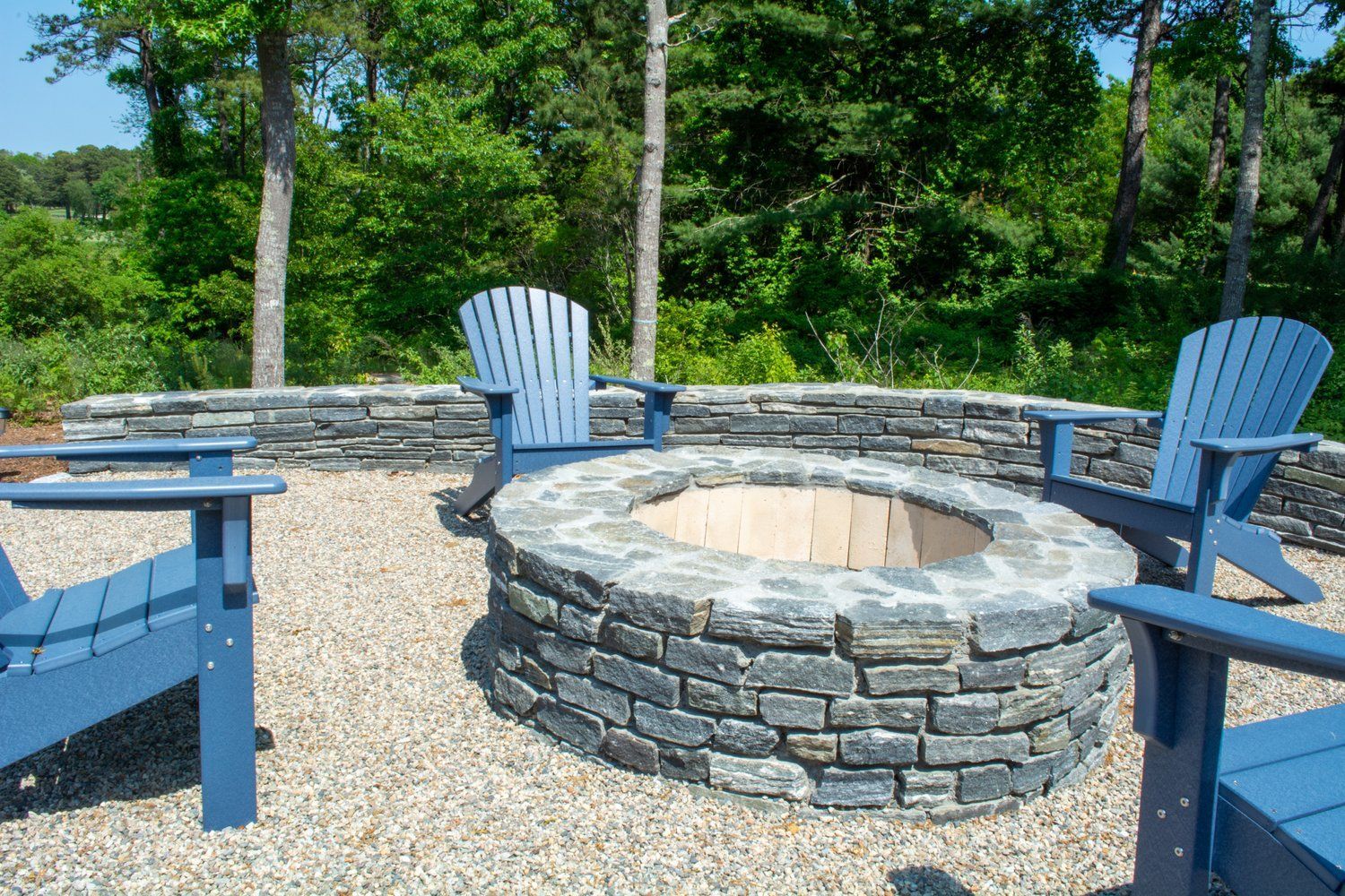 A fire pit is surrounded by blue chairs on a gravel patio.