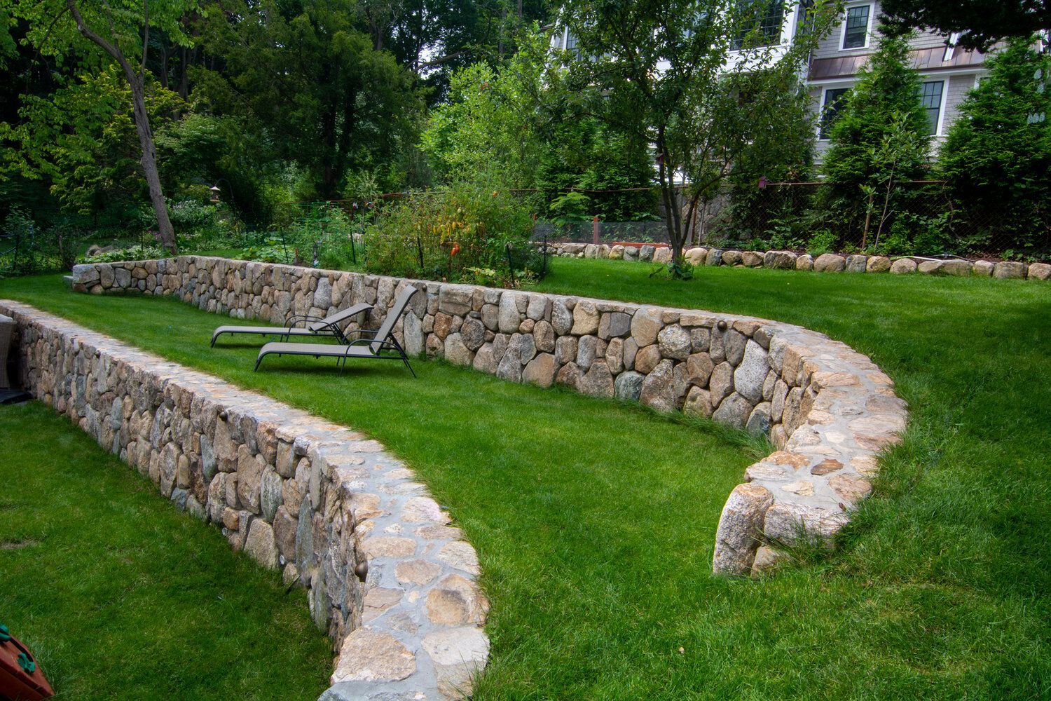 A stone wall surrounds a lush green lawn in a backyard.