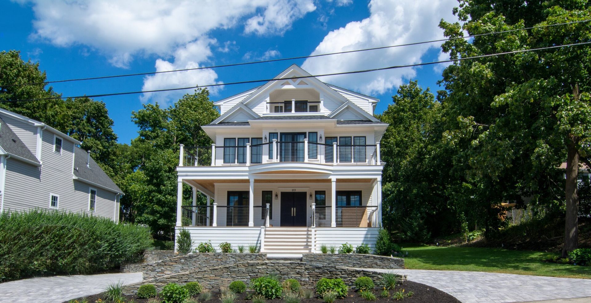 A large white house with a large porch is surrounded by trees.