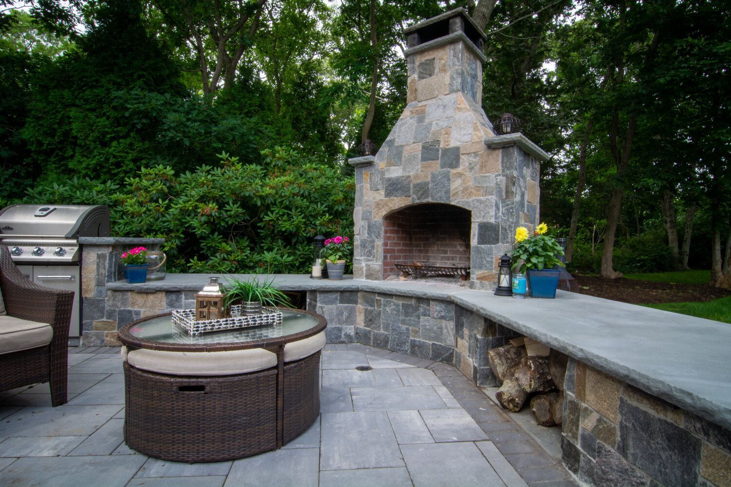 A patio with a fireplace , table , chairs and a grill.