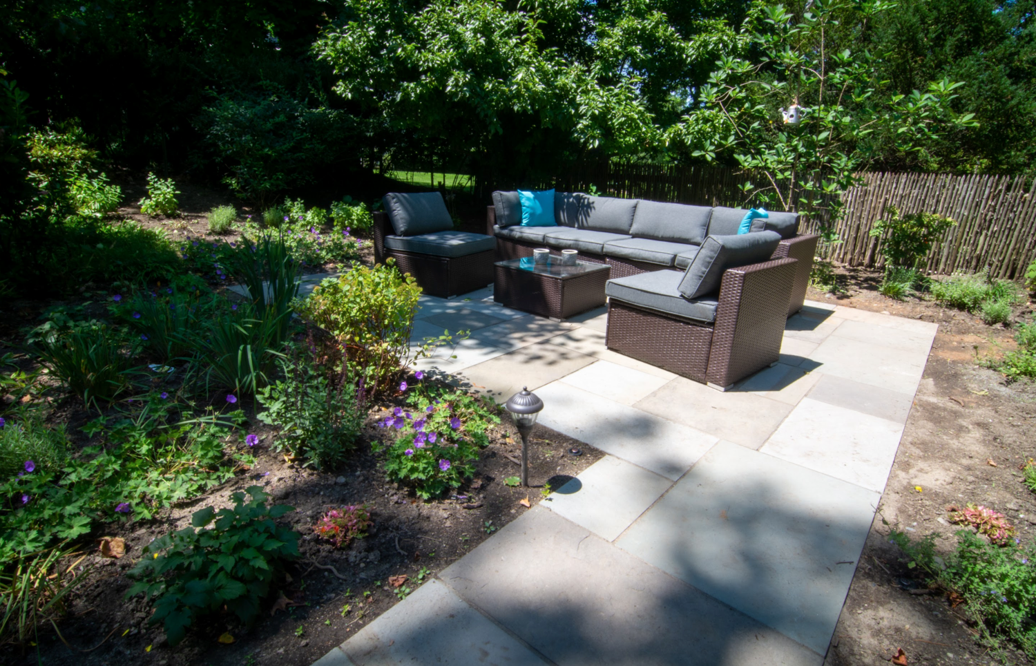 A patio with a couch and chairs in the middle of a garden.