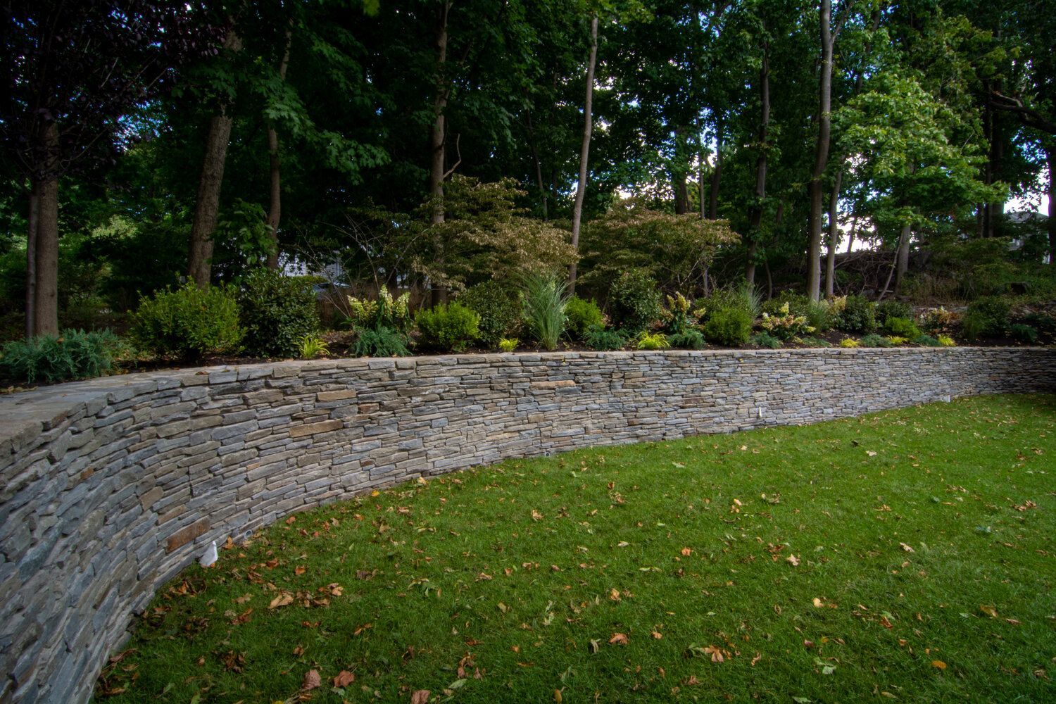 A stone wall surrounds a lush green lawn in a park.