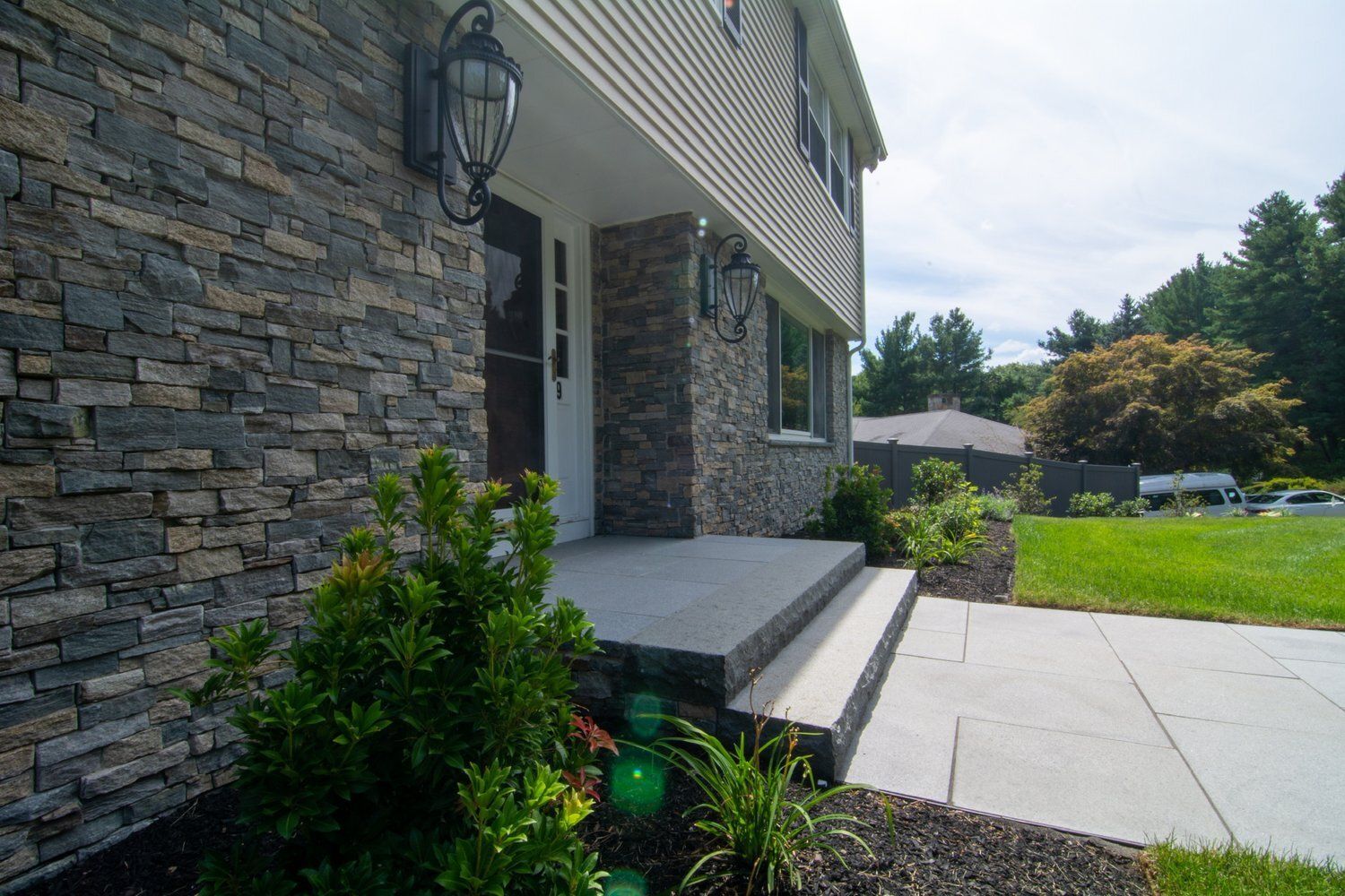 The front of a house with a stone wall and a walkway leading to it.