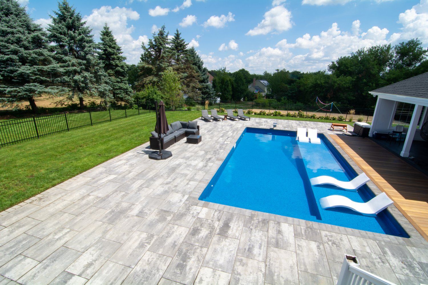 A large swimming pool is surrounded by a patio and chairs.