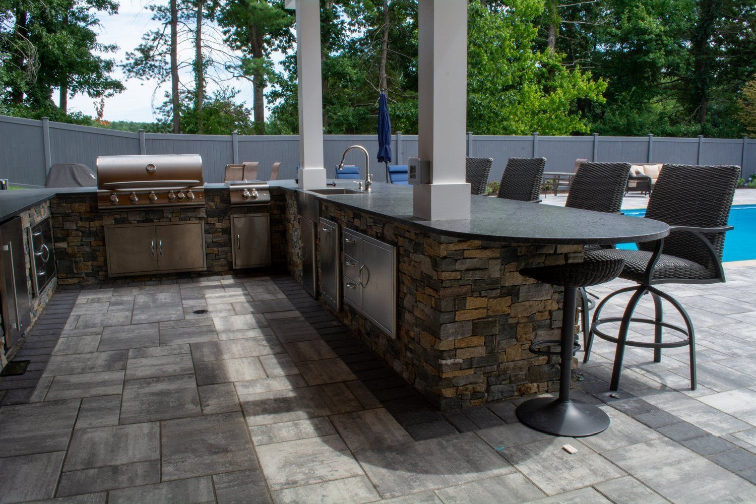 A large outdoor kitchen with a grill , table and chairs next to a pool.