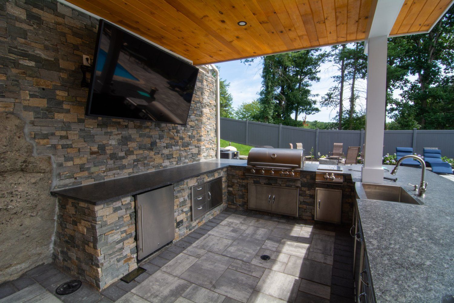 A large outdoor kitchen with a grill , sink , and television.