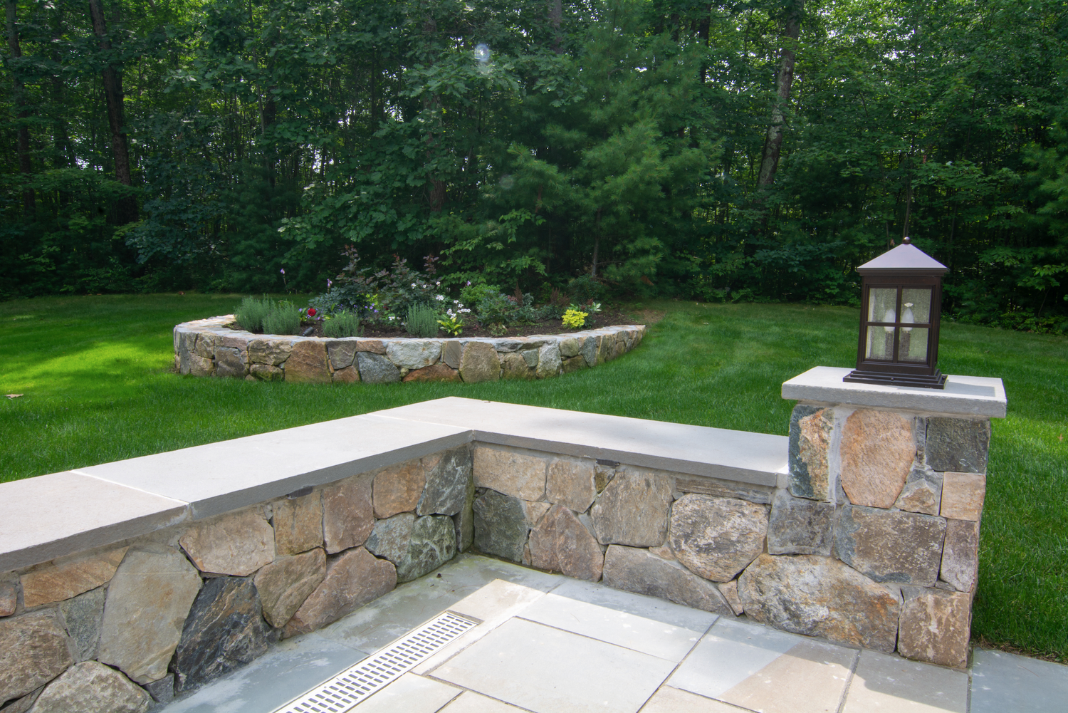 A stone wall with a lantern on top of it in a backyard.