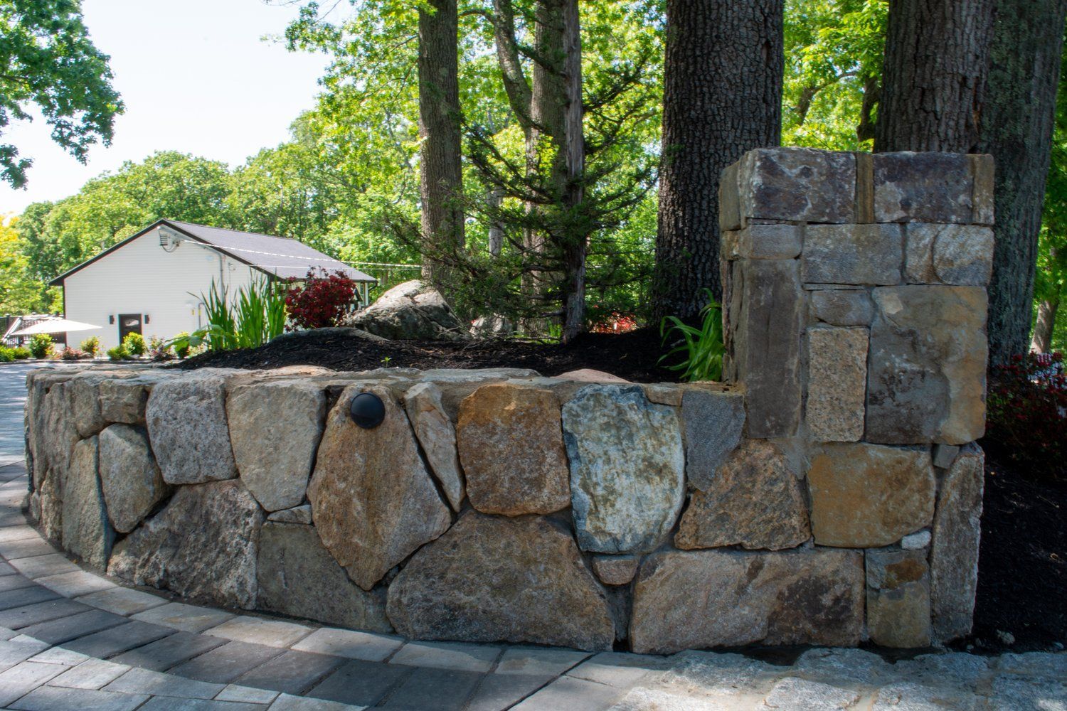 A stone wall with trees in the background and a house in the background