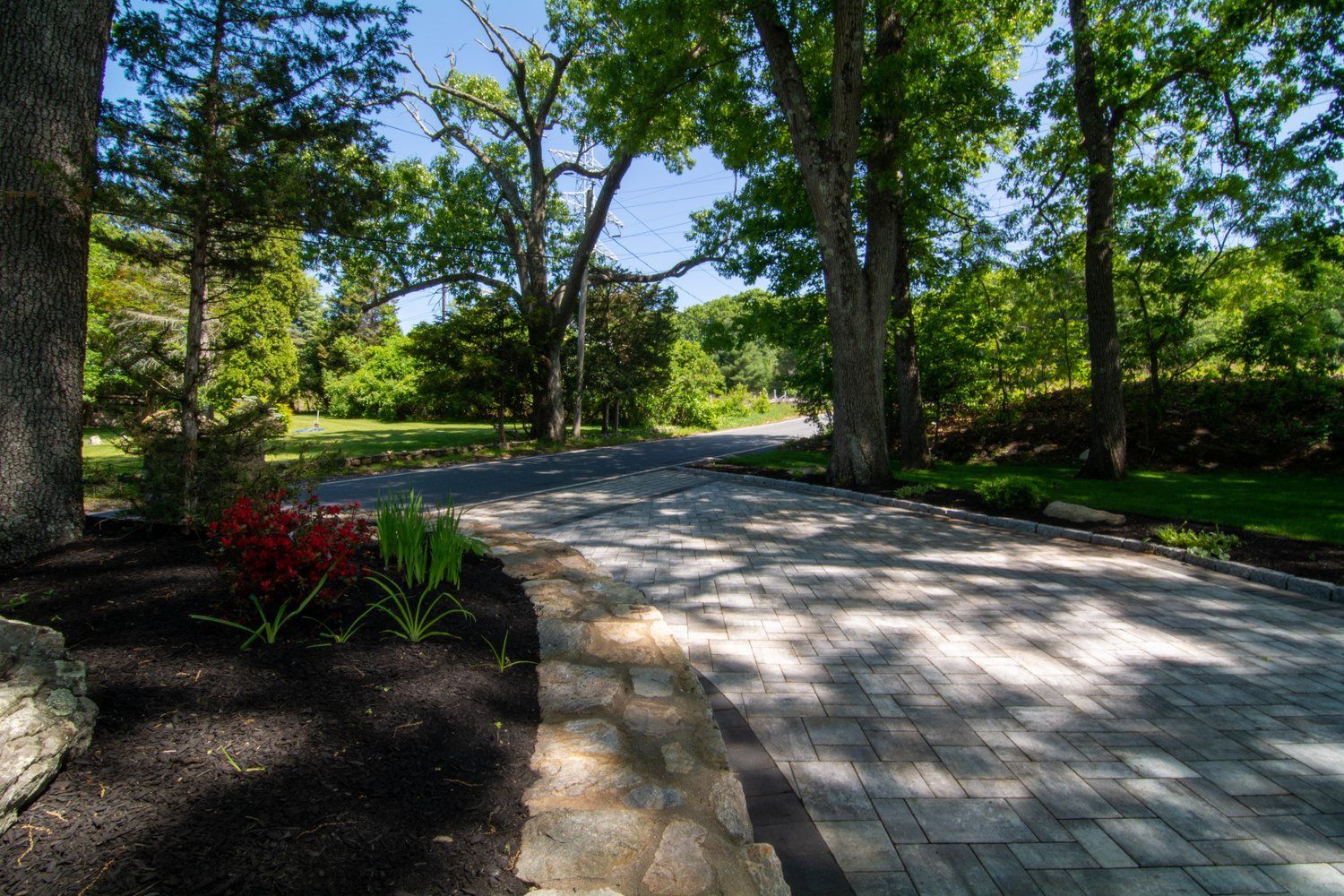 A brick driveway leading to a lush green field surrounded by trees.