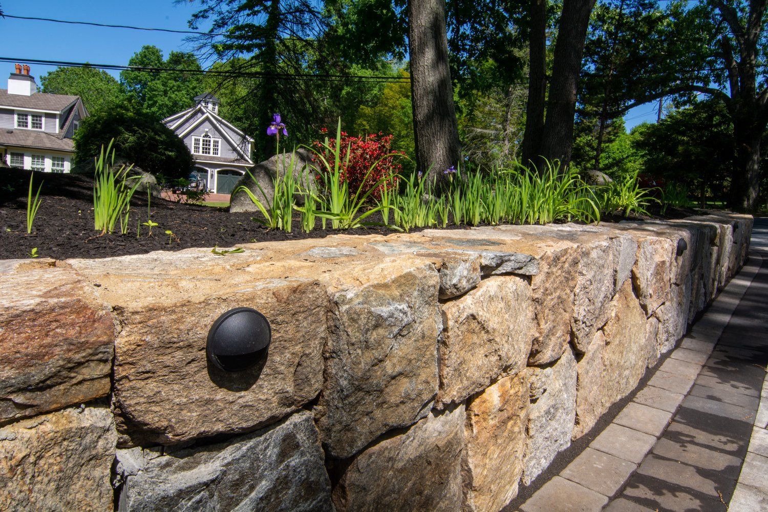 A stone wall with a black light on it and a house in the background.