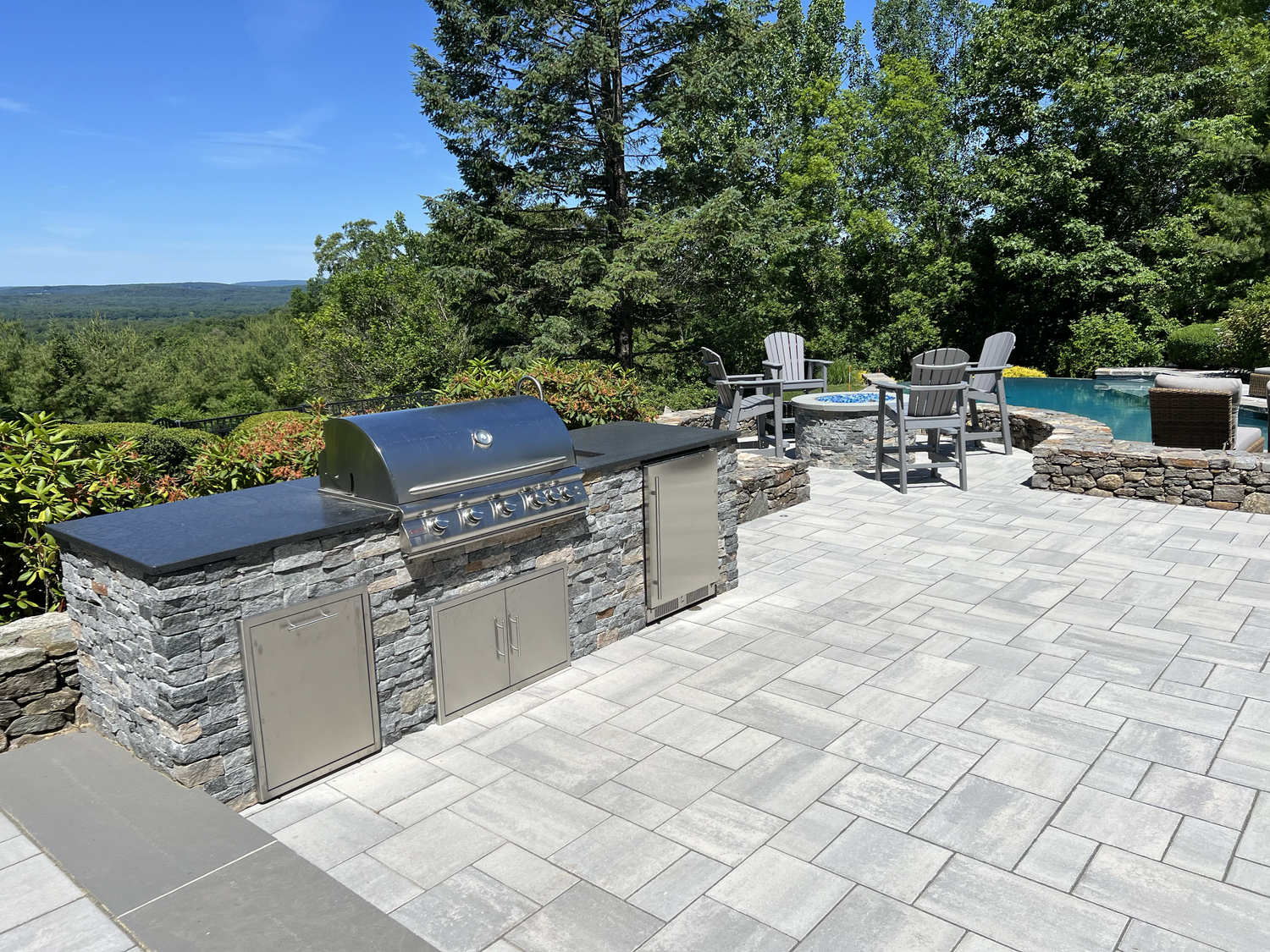 A patio with a grill and a pool in the background.