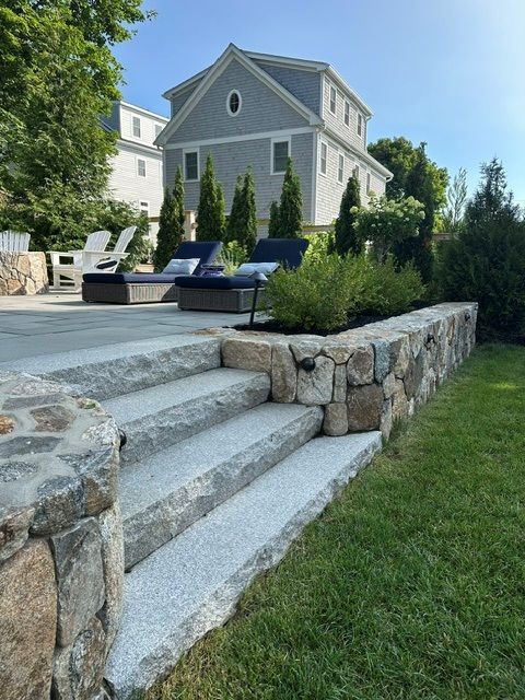 Stone steps lead to a landscaped yard with lounge chairs and a white house in the background