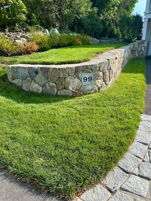 Stone retaining wall with house number 99 beside a green lawn and garden path