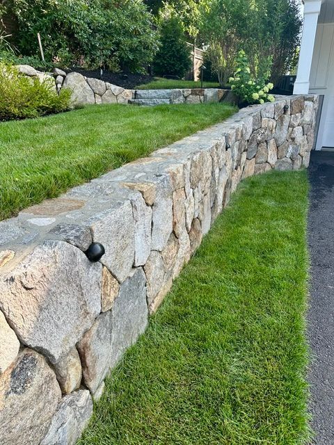 Stone retaining wall beside a neatly trimmed green lawn in a landscaped yard