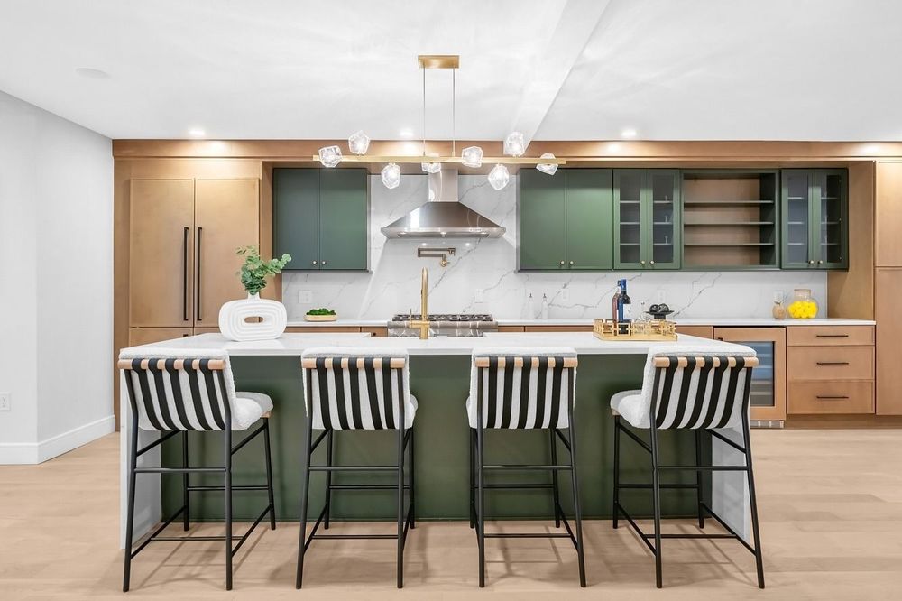 A kitchen with green cabinets , white counter tops , and striped bar stools.