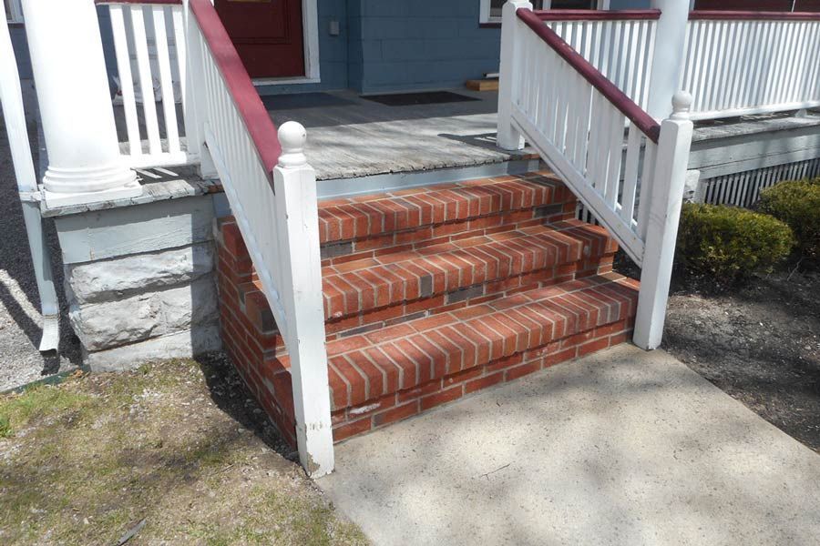 A set of brick stairs leads up to a porch with a white railing