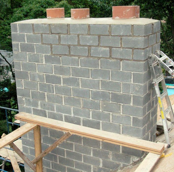 A brick chimney is being built with a ladder behind it