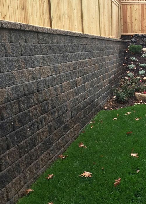 A large brick wall is surrounded by grass and a wooden fence