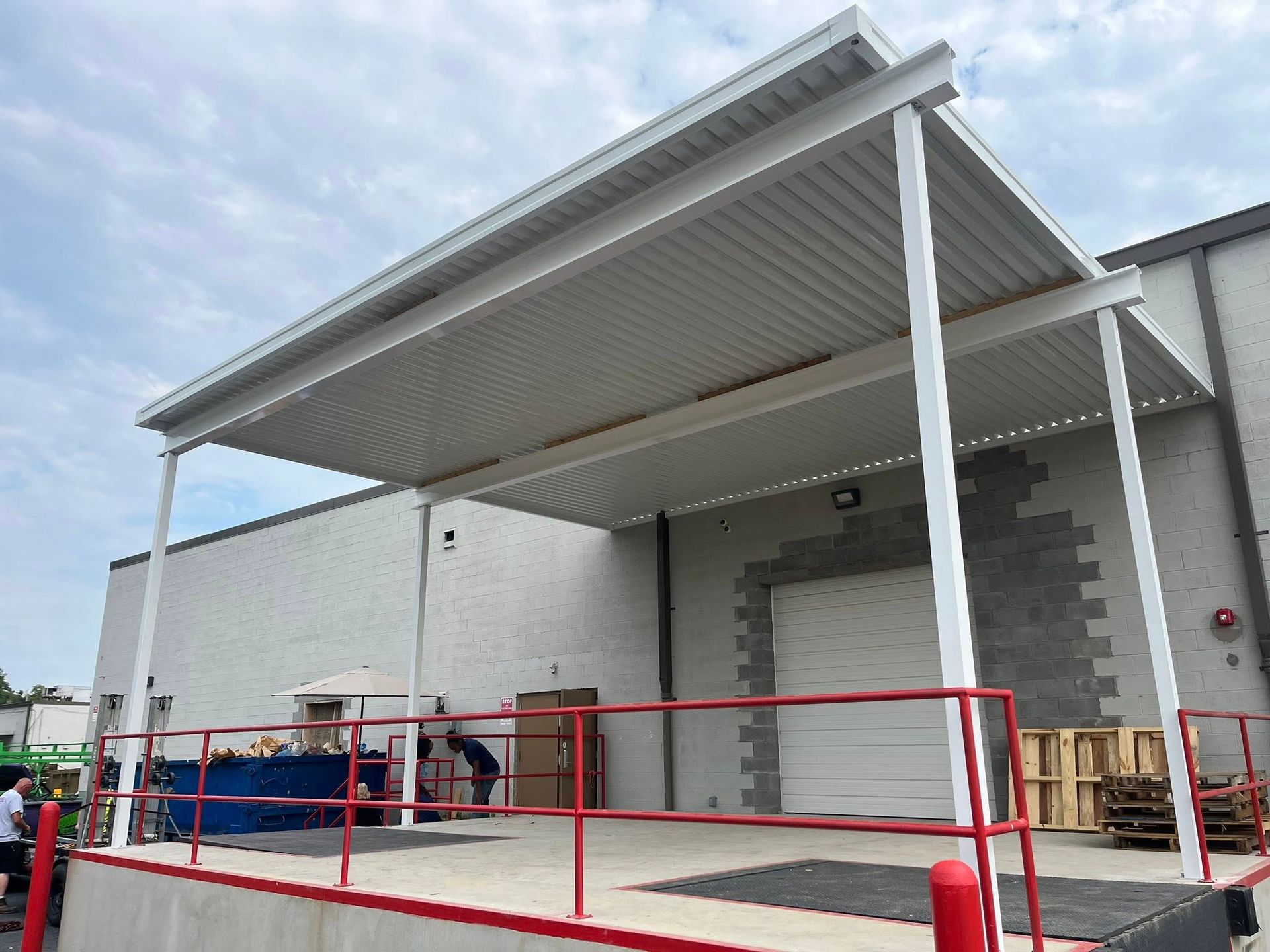White industrial loading dock with a metal canopy roof and a red safety railing against a white brick building.