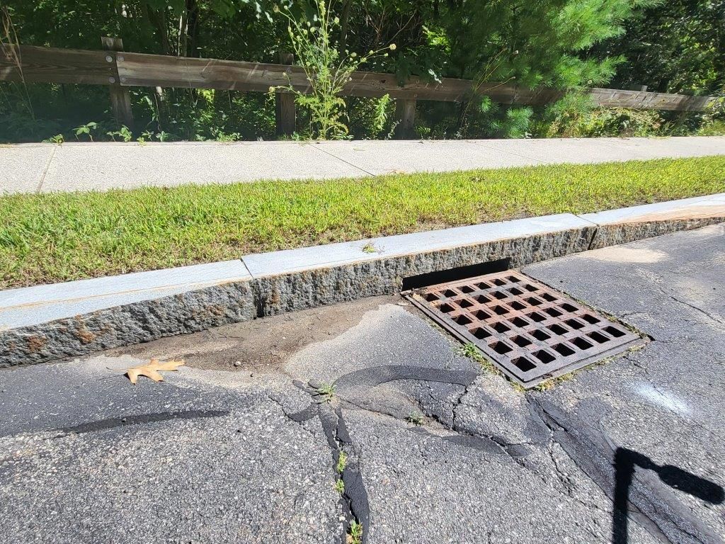 A manhole cover on the side of a road next to a sidewalk.
