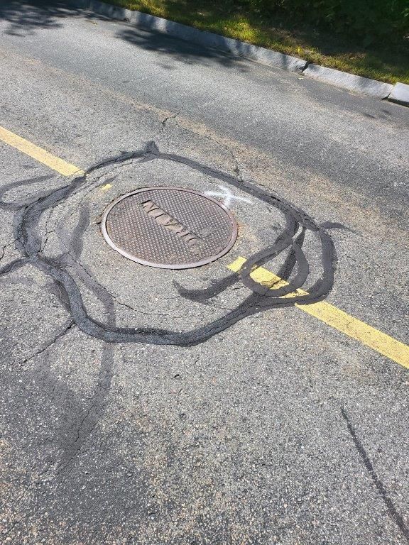 A manhole cover is sitting on the side of the road next to a yellow line.