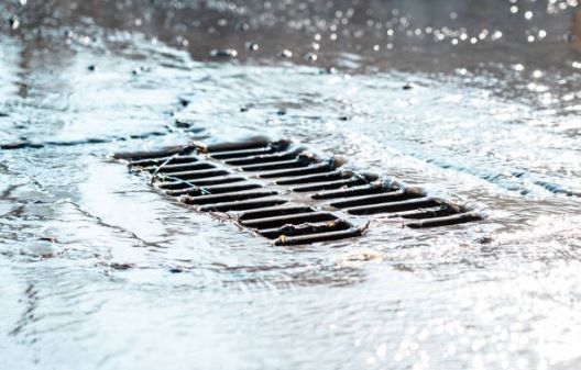 A manhole cover is covered in snow and water on a rainy day.