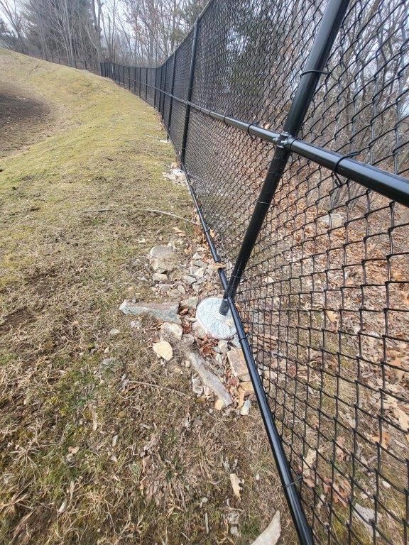 A black chain link fence surrounds a grassy hillside.