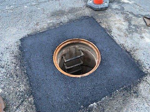 A manhole cover with a hole in it and leaves on the ground.