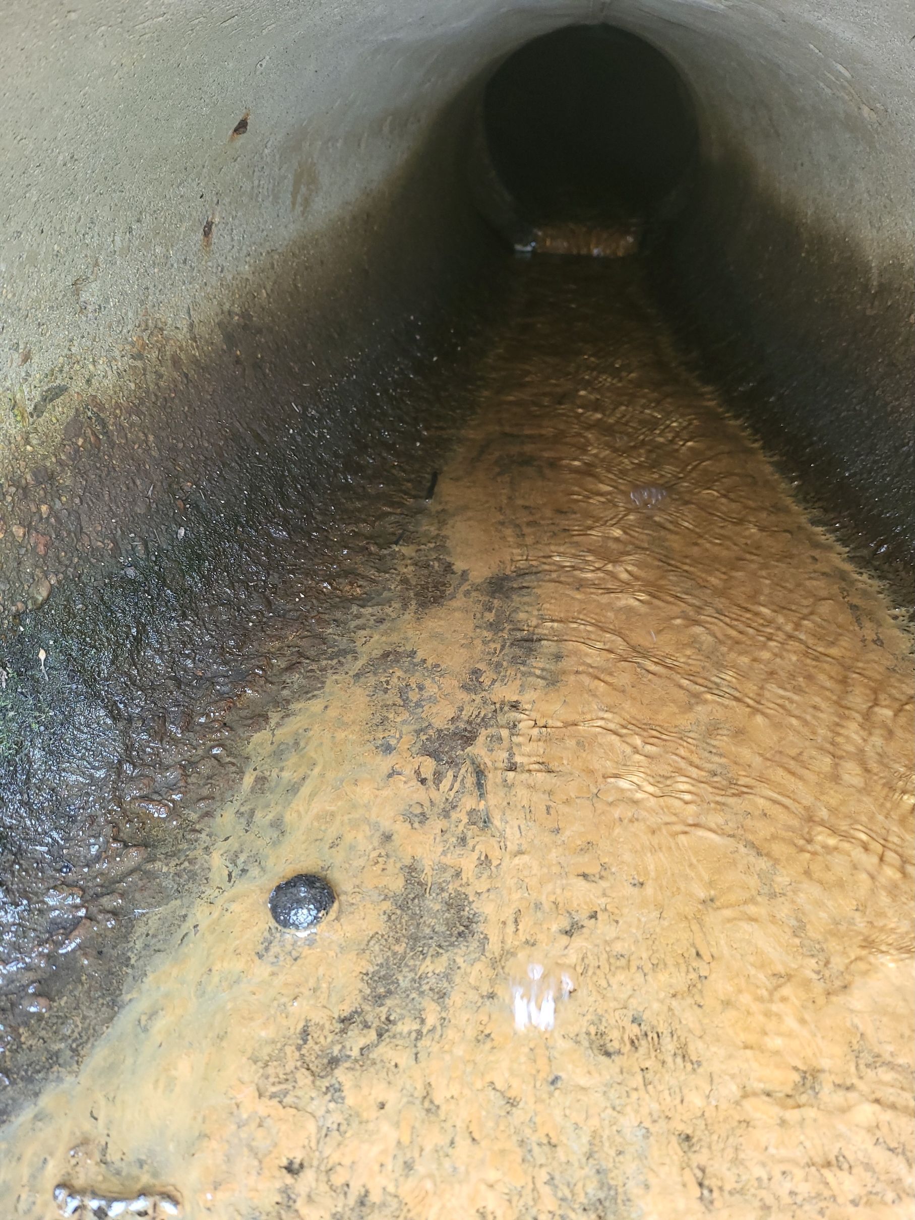 A close up of a muddy pipe with water coming out of it.