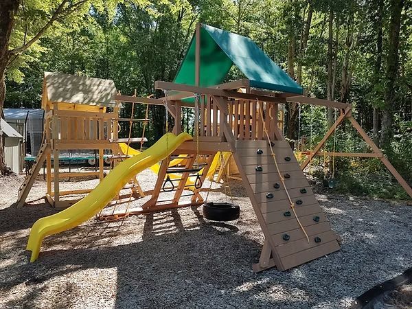 Playground with swings, slides, and climbing structures on a grassy area, under a blue sky.