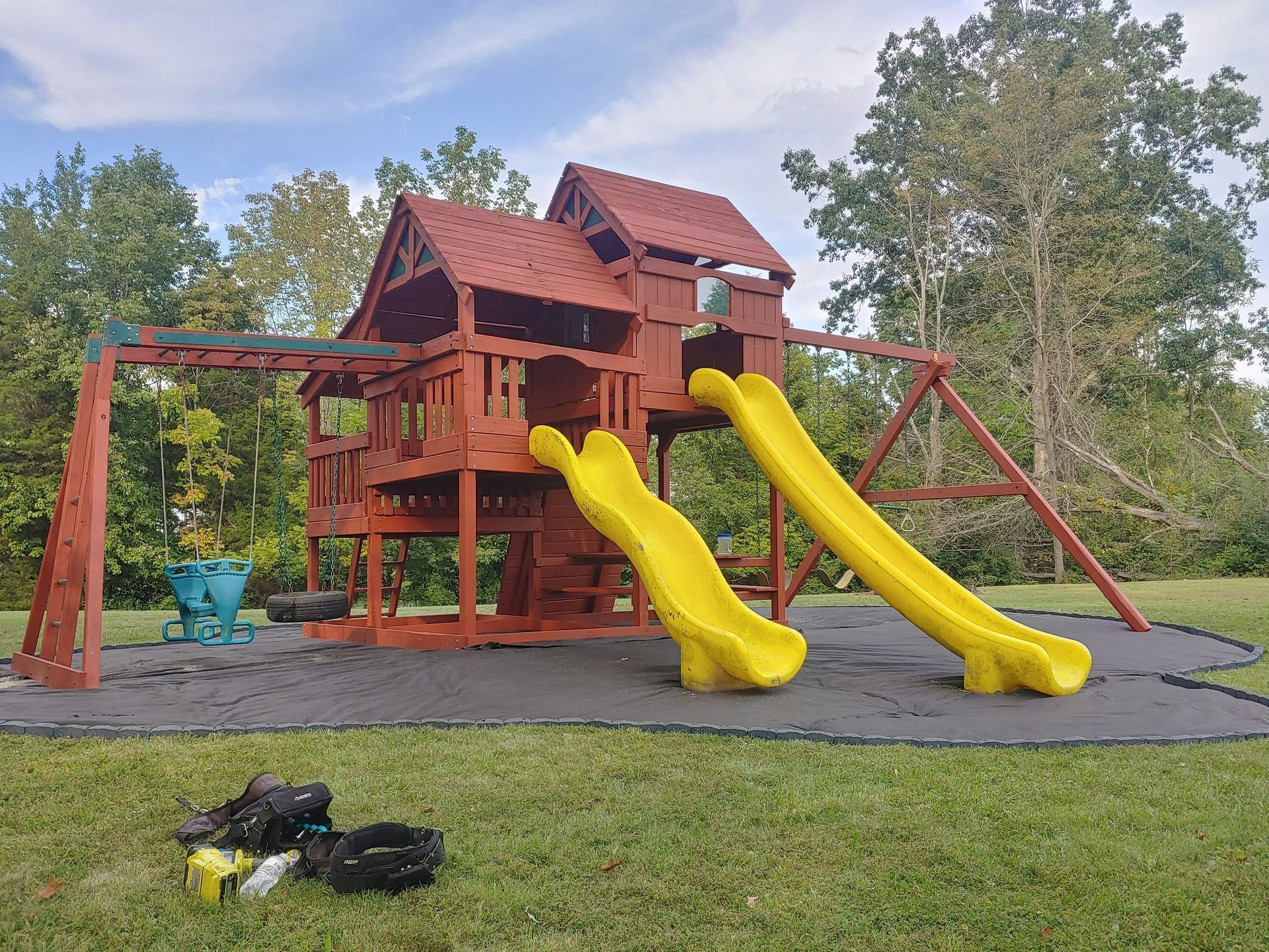 Playground with wooden structure, two slides, swing set, and black rubber safety surfacing.