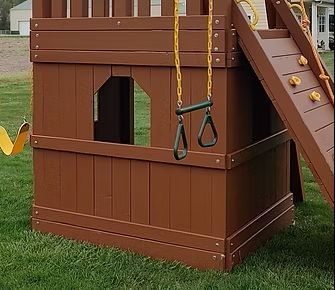 Brown wooden playset with a swing set and a climbing wall on green grass.