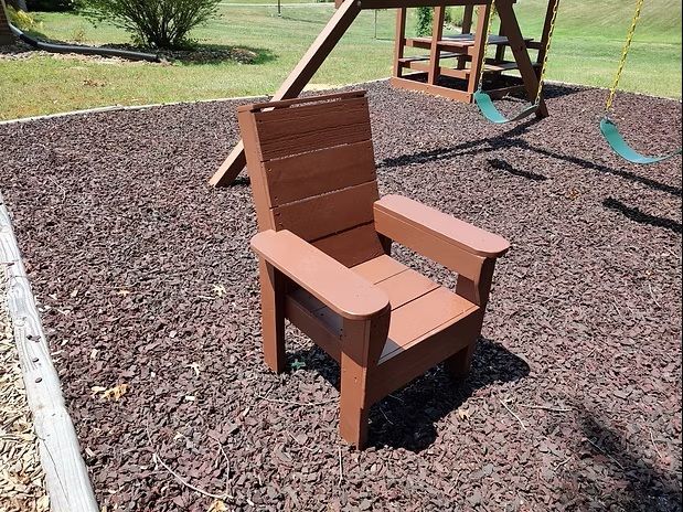 Brown plastic Adirondack chair on mulch in a playground.