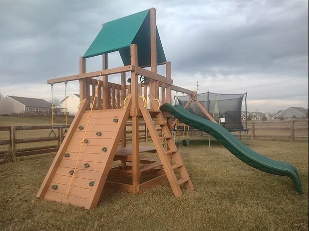 Wooden playset with climbing wall, slide, and swing set in a grassy backyard.