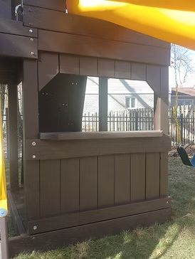 Brown wooden playhouse with a window and a yellow slide on a grassy lawn.