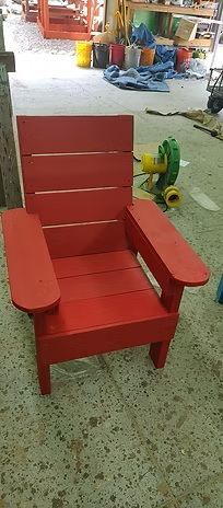 Red wooden Adirondack chair in a workshop setting.