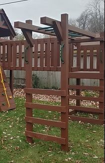 Wooden playground set with ladder, monkey bars, and platforms in a yard.