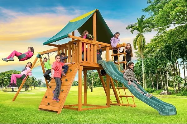 Children playing on a wooden outdoor playset with slide, swings, and climbing wall.