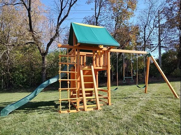 Wooden backyard playset with a green slide, rope ladder, and swings.